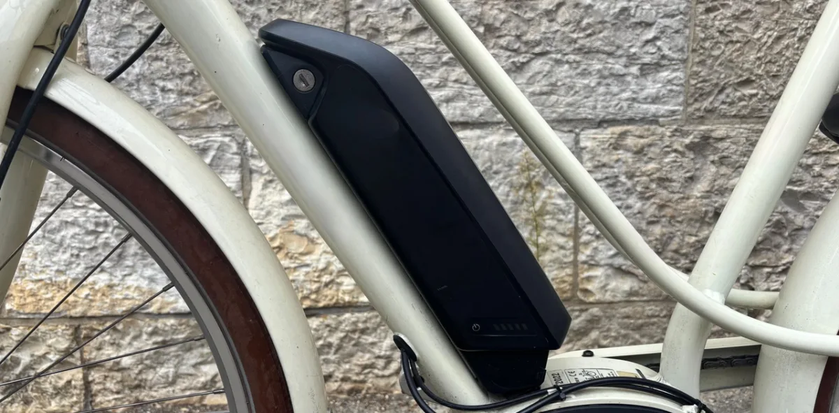 Das Bild zeigt den Rahmen eines E-Bikes in Nahaufnahme. Der schwarze Akku ist in den weißen Rahmen integriert und an einem Steinwandhintergrund zu sehen.