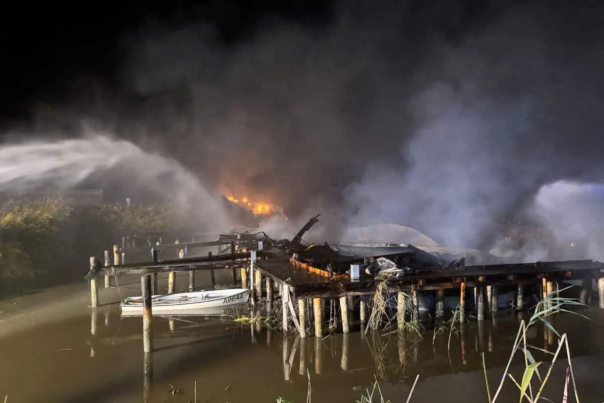 In der Nacht wird ein brennender Steg an einem Fluss von der Feuerwehr gelöscht. Rauch steigt auf, während Flammen sichtbar sind.