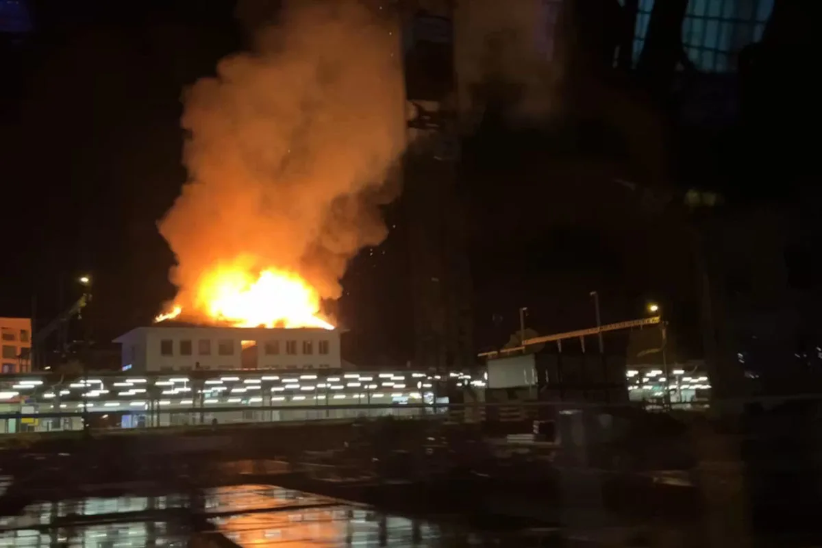 Ein Gebäude steht bei Nacht in Flammen, aus dem Dach steigt dichter Rauch auf. Die Umgebung ist dunkel erleuchtet.