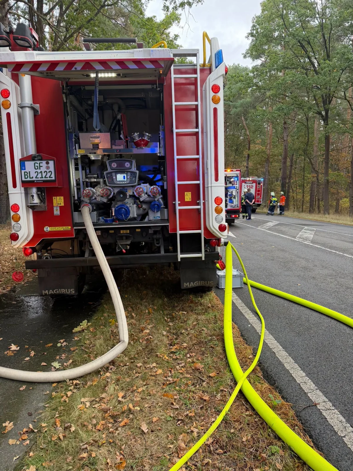 Ein rotes Feuerwehrfahrzeug steht am Straßenrand, Schläuche sind ausgelegt und mit dem Fahrzeug verbunden.