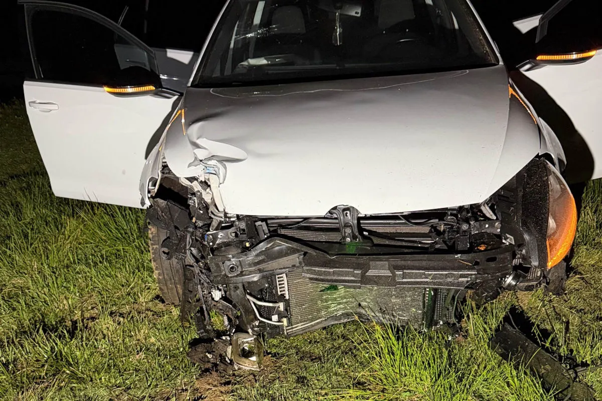 Ein weißes Auto mit erheblichen Frontschäden steht im Gras, die Fahrertür ist geöffnet. Aufnahme bei Nacht.