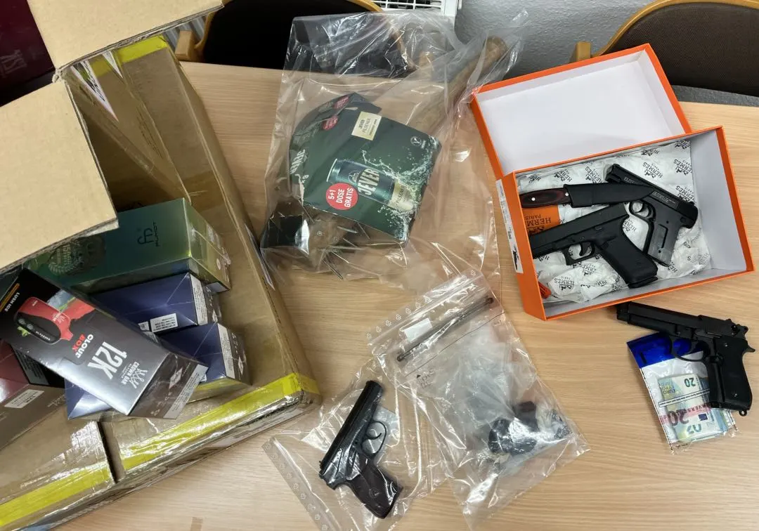Auf einem Tisch liegen mehrere Plastiktüten mit Waffen, daneben Kartons und sichtbares Bargeld.