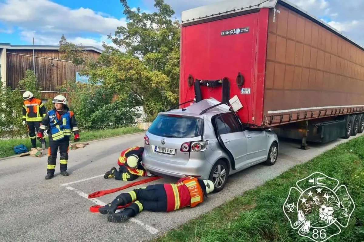 Ein silberner VW steckt hinten unter einem roten Lkw-Anhänger fest. Mehrere Rettungskräfte arbeiten an der Unfallstelle auf einer Landstraße.