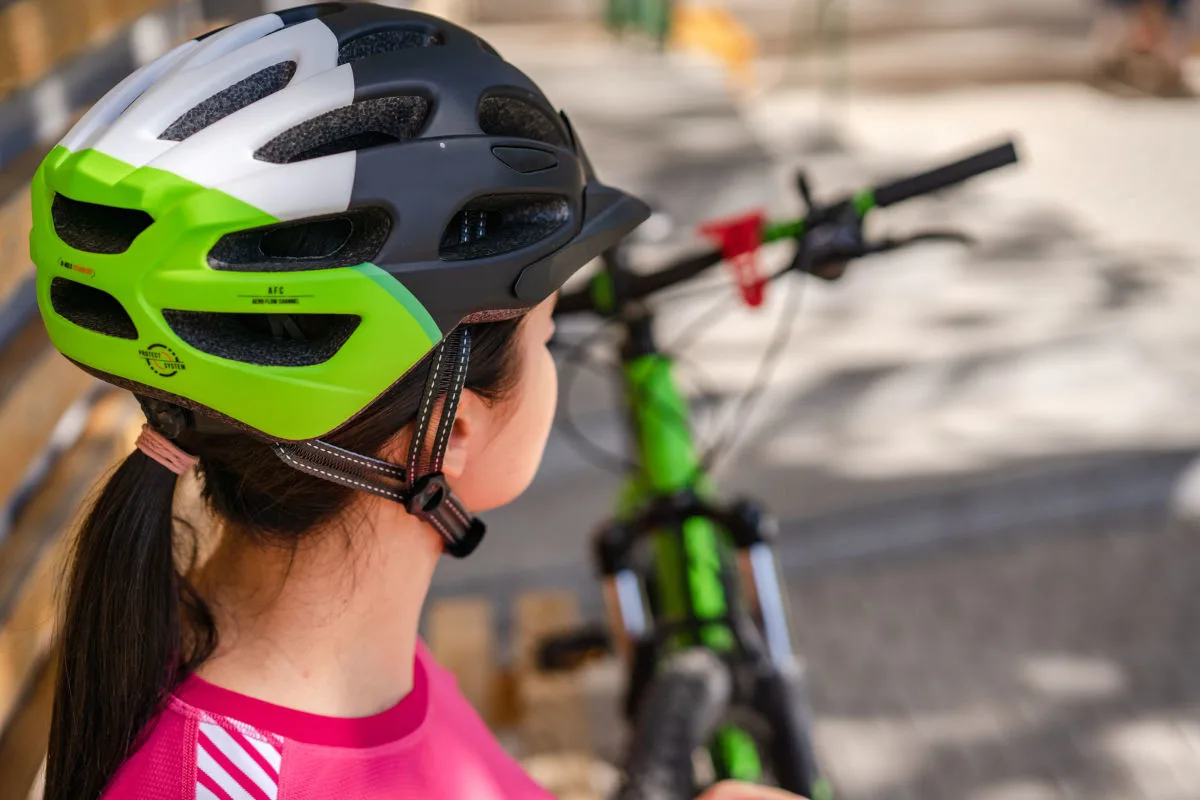 Eine Person trägt einen grün-schwarzen Fahrradhelm und sitzt auf oder neben einem grünen Fahrrad. Der Hintergrund ist unscharf.