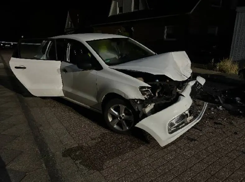 Ein weißes Auto mit geöffneter Fahrertür steht mit stark beschädigter Front auf einer Wohnstraße. Die Aufnahme wurde bei Dunkelheit gemacht.