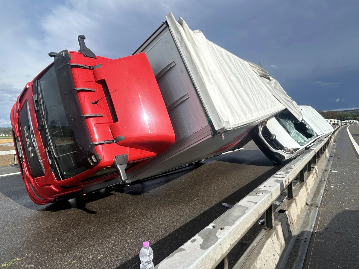 Ein roter Lastwagen ist auf der Seite umgestürzt, der weiße Aufbau ist beschädigt. Der Unfall ereignete sich auf der Autobahn.
