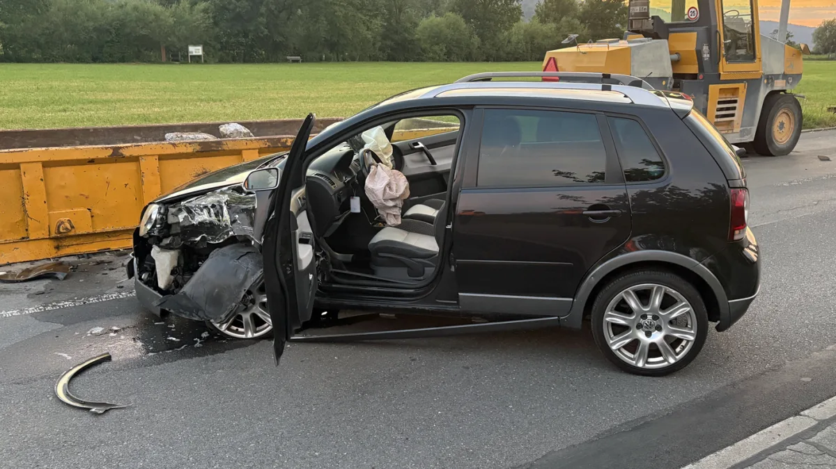 Ein schwarzer VW steht mit erheblichem Frontschaden an einer gelben Leitplanke. Der Airbag ist ausgelöst.