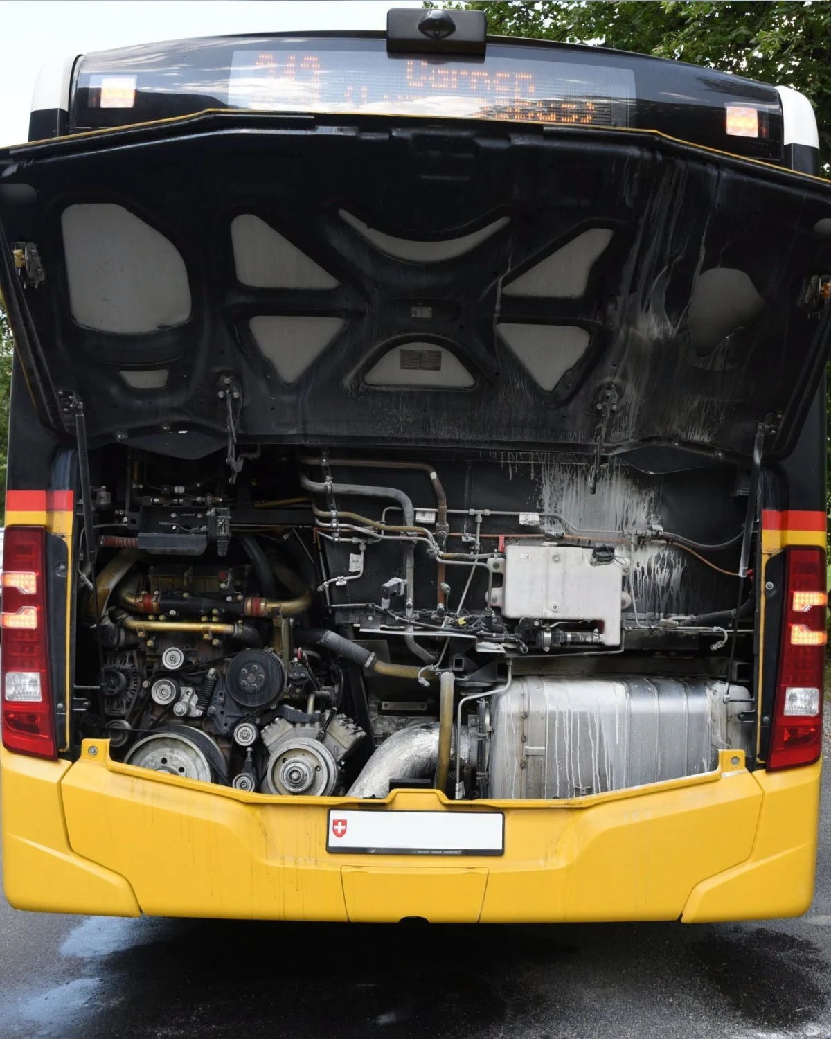 Ein gelber Linienbus steht mit geöffneter Motorabdeckung auf einer Straße. Teile des Motors und eine Flüssigkeit sind sichtbar.