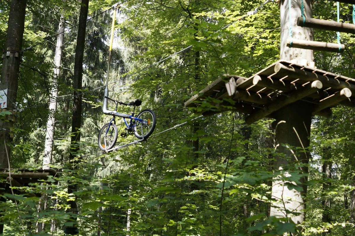 Ein Fahrrad hängt an einem Seil zwischen zwei Plattformen in einem dichten Wald-Kletterpark.