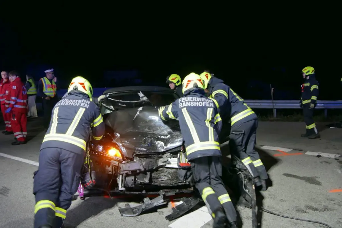 Mehrere Feuerwehrleute von Ranshofen arbeiten bei Nacht an einem Auto mit stark beschädigter Front auf einer Straße.