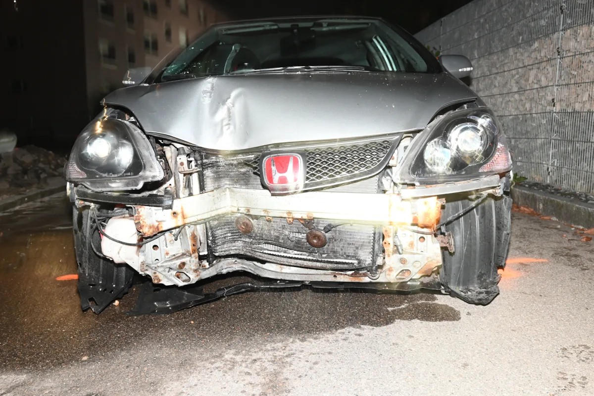 Die Front eines silbernen Honda zeigt schwere Unfallspuren mit beschädigtem Kühlergrill und Scheinwerfer. Der Unfall ereignete sich nachts in einem urbanen Bereich vor einer Hauswand.