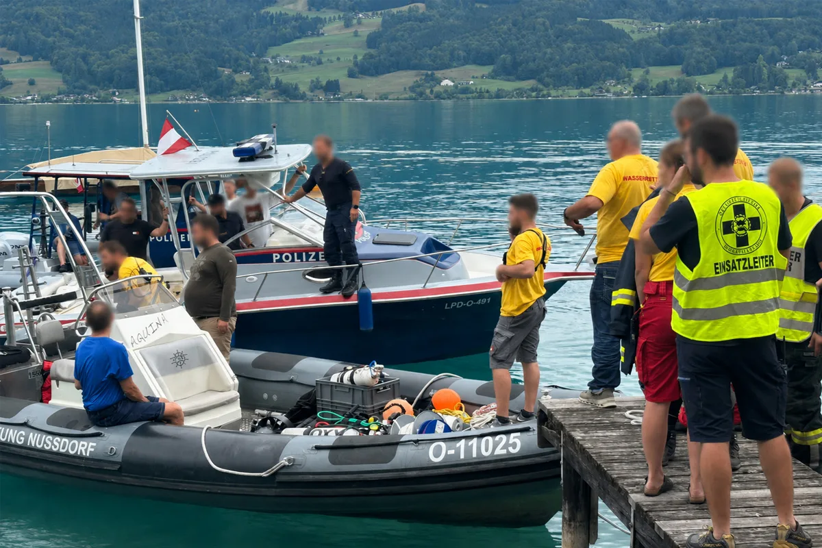 Ein Polizeiboot und mehrere Rettungskräfte versammeln sich an einem Seeufer. Personen tragen Einsatzwesten.