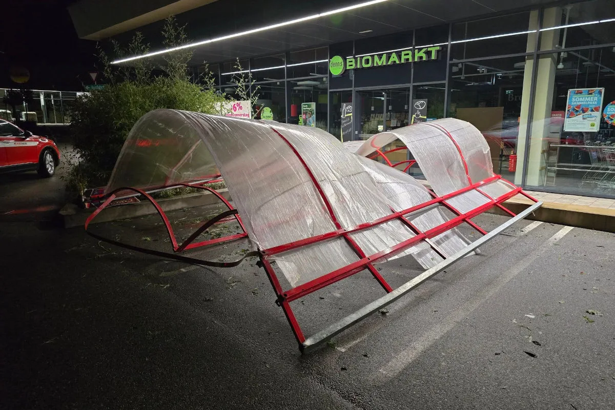 Ein umgestürzter roter Fahrradunterstand liegt vor einem Biomarkt bei Nacht. Im Hintergrund ist ein rotes Auto sichtbar.