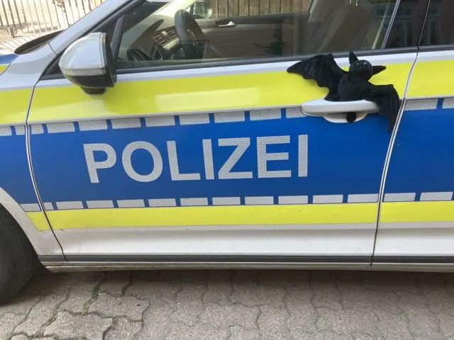 Ein Polizeiwagen mit einem blauen und gelben Streifen. An der Tür hängt ein schwarzes Plüschtier.