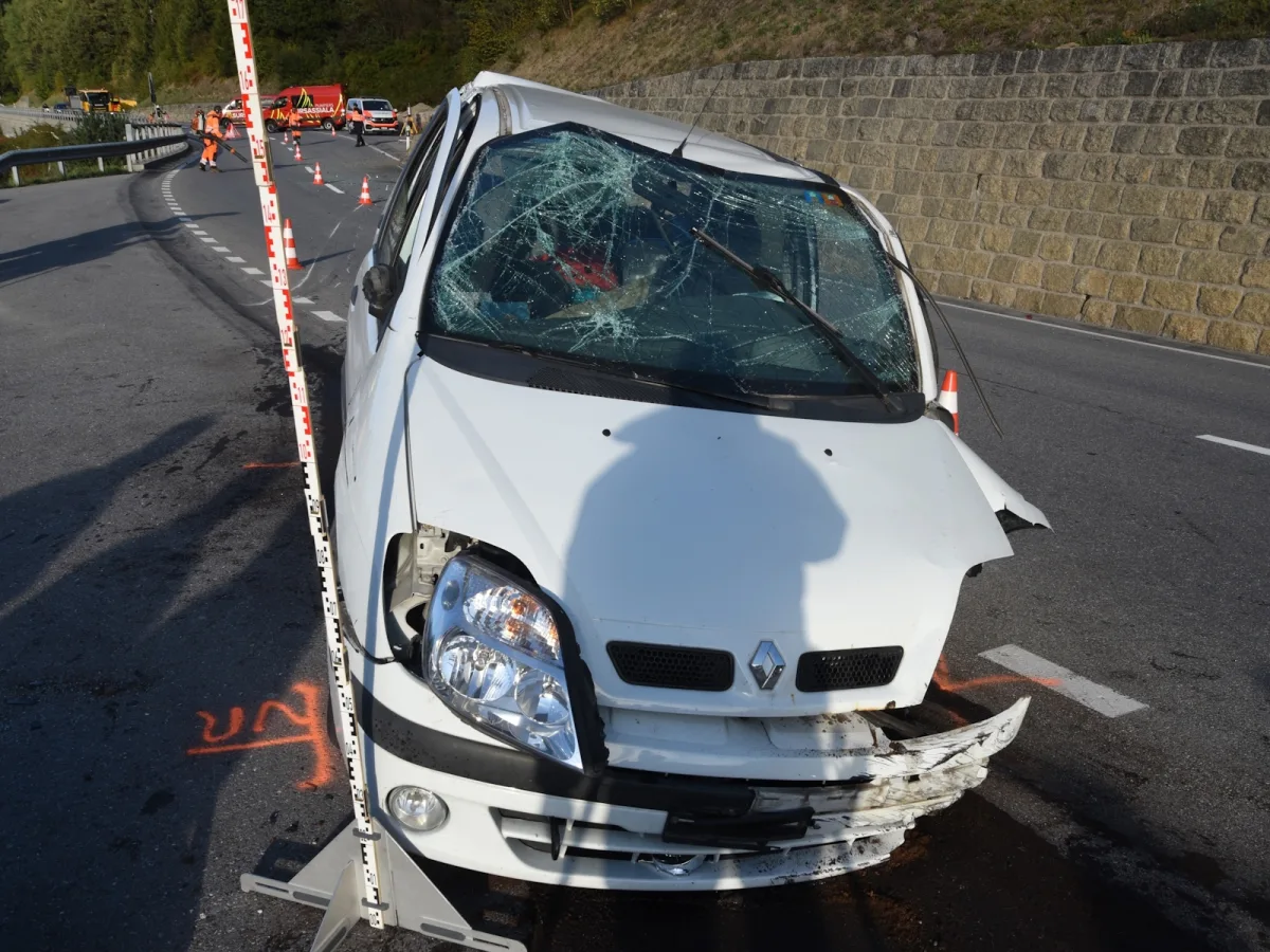Ein weißer Renault mit eingeschlagener Windschutzscheibe steht beschädigt auf einer Straße. Polizei und Absperrungen sind im Hintergrund zu sehen.