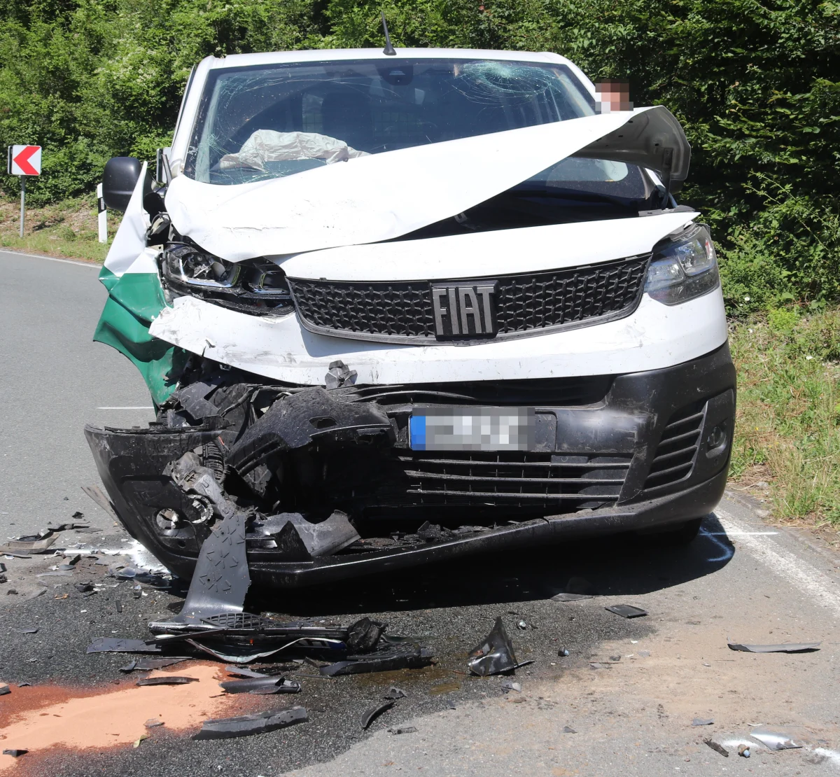Ein weißer Fiat mit stark eingedrückter und beschädigter Vorderseite steht auf einer Landstraße. Trümmerteile liegen vor dem Fahrzeug auf der Fahrbahn.