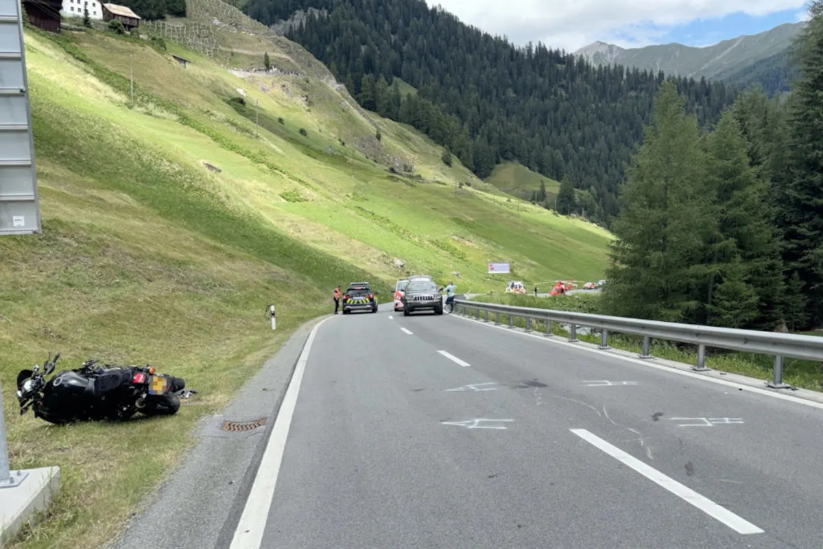 Ein beschädigtes Motorrad liegt abseits einer kurvigen Alpenstraße in den Bergen, während Polizeifahrzeuge die Straße sichern.