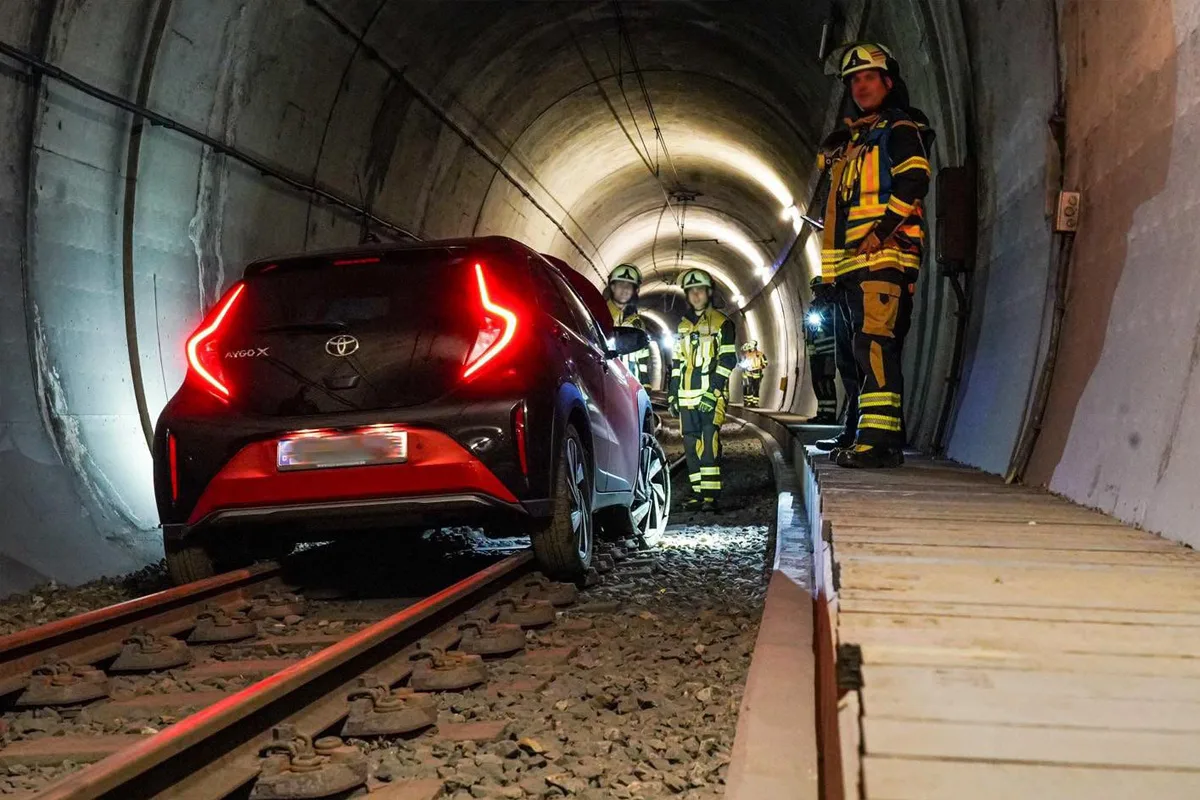 Ein schwarzes Auto steht im Tunnel auf Eisenbahnschienen, umgeben von mehreren Feuerwehrleuten in Einsatzkleidung.