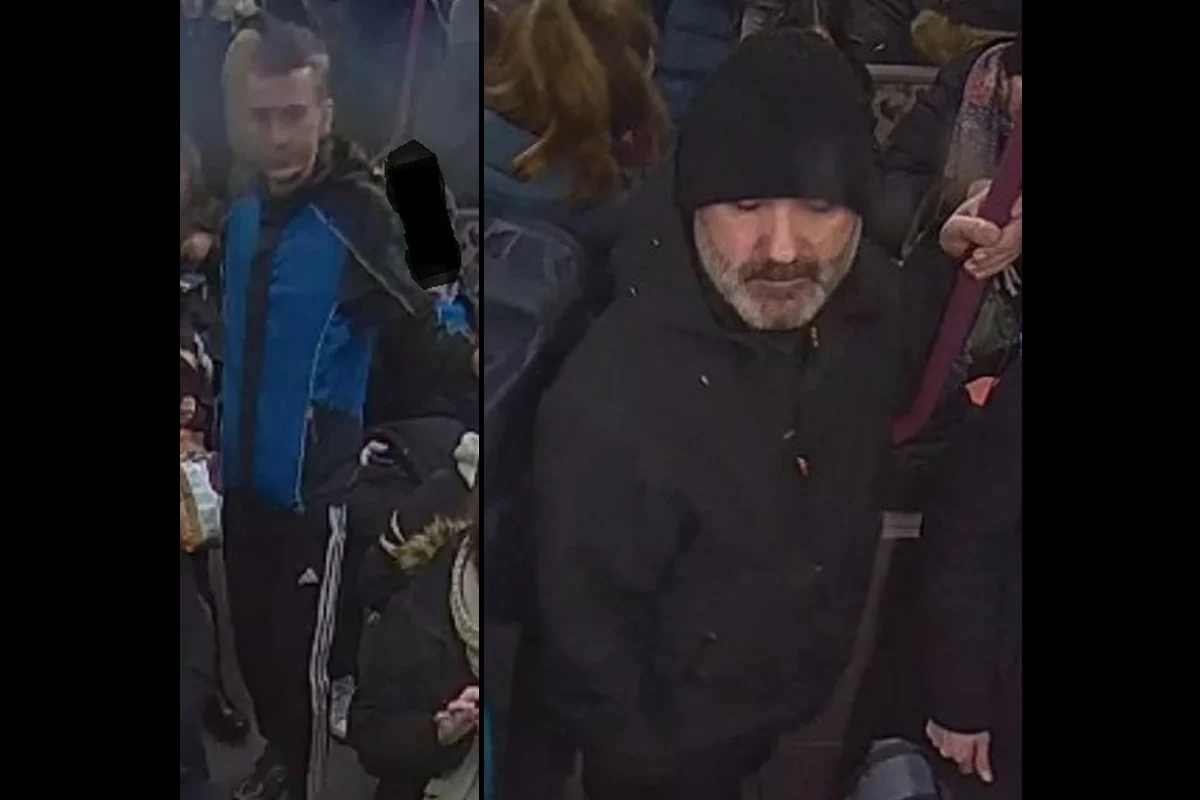 Zwei Männer stehen in einem vollen öffentlichen Verkehrsmittel. Der linke Mann trägt eine blaue Jacke, der rechte eine schwarze Mütze.