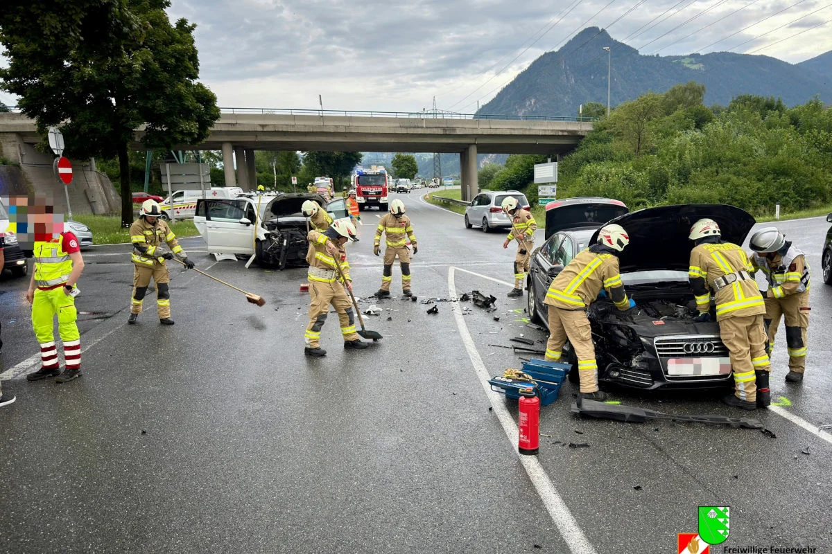 Mehrere Feuerwehrleute in Schutzkleidung arbeiten an zwei kollidierten Fahrzeugen auf einer Straße unter einer Brücke.