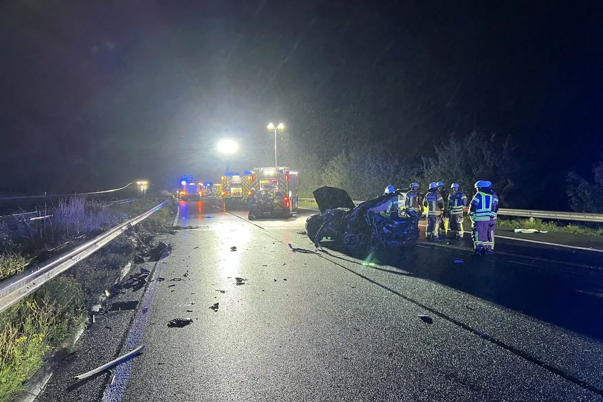 Mehrere Einsatzfahrzeuge beleuchten eine nächtliche Unfallstelle auf der Autobahn, während Feuerwehrleute das beschädigte Fahrzeug begutachten.