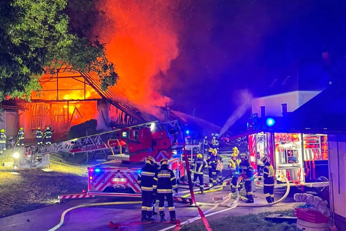 Mehrere Feuerwehrleute bekämpfen einen großen Brand in einem Gebäude bei Nacht. Löschfahrzeuge und Schläuche sind im Einsatz.