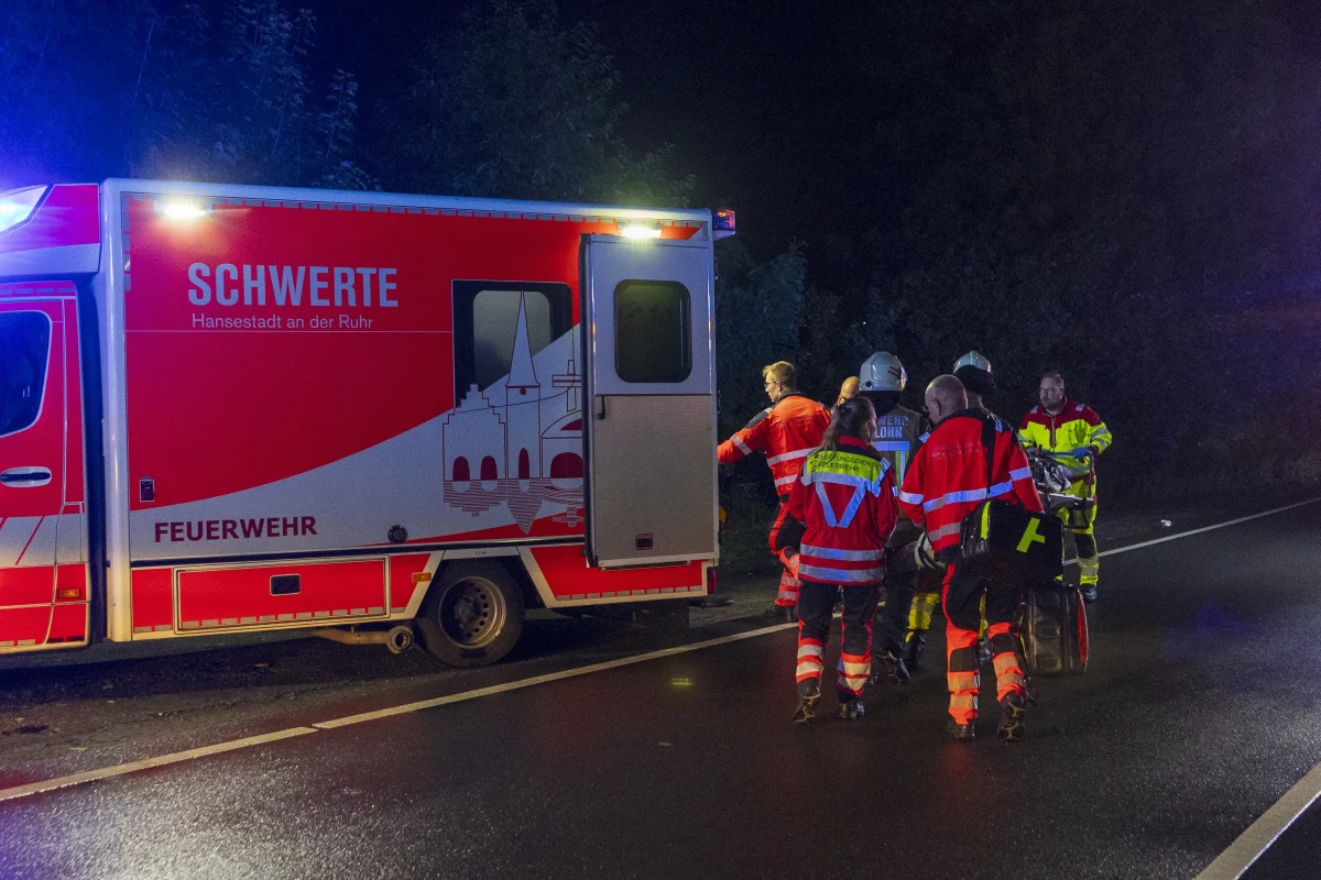 Ein rotes Einsatzfahrzeug der Feuerwehr Schwerte steht auf einer Landstraße, umgeben von mehreren Feuerwehrleuten in Einsatzkleidung bei Nacht.