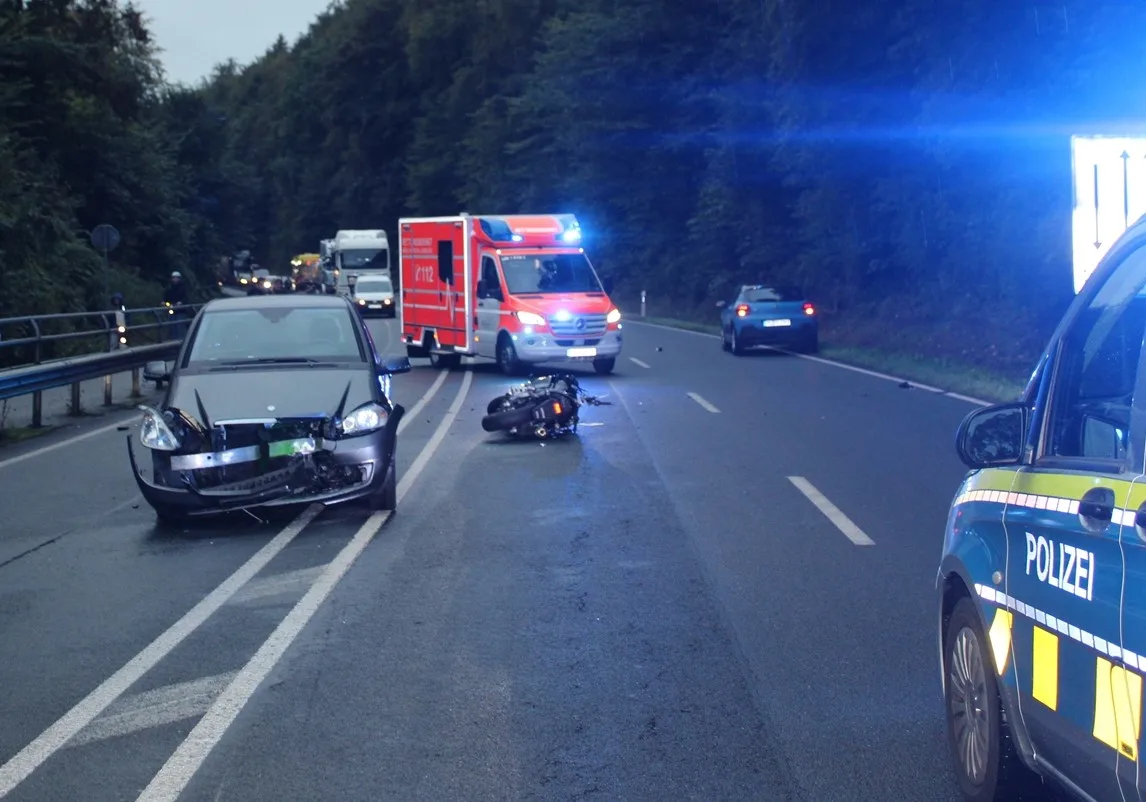 Ein Unfall ereignete sich auf einer Landstraße, bei dem ein Auto und ein Motorrad stark beschädigt wurden. Ein Polizeiwagen und ein Rettungswagen sind vor Ort anwesend.