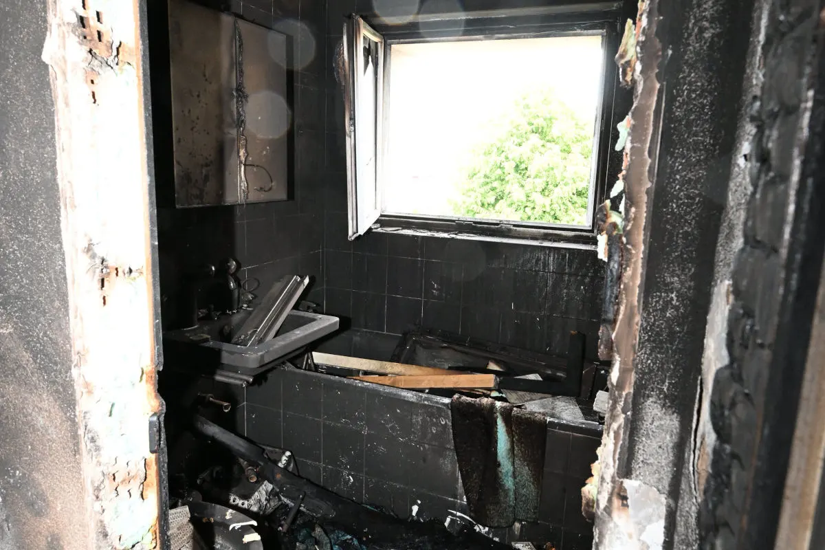Das Bild zeigt ein verbranntes Badezimmer mit Ruß an den Wänden. Ein Fenster ist offen und durch das Fenster ist ein grüner Baum sichtbar.