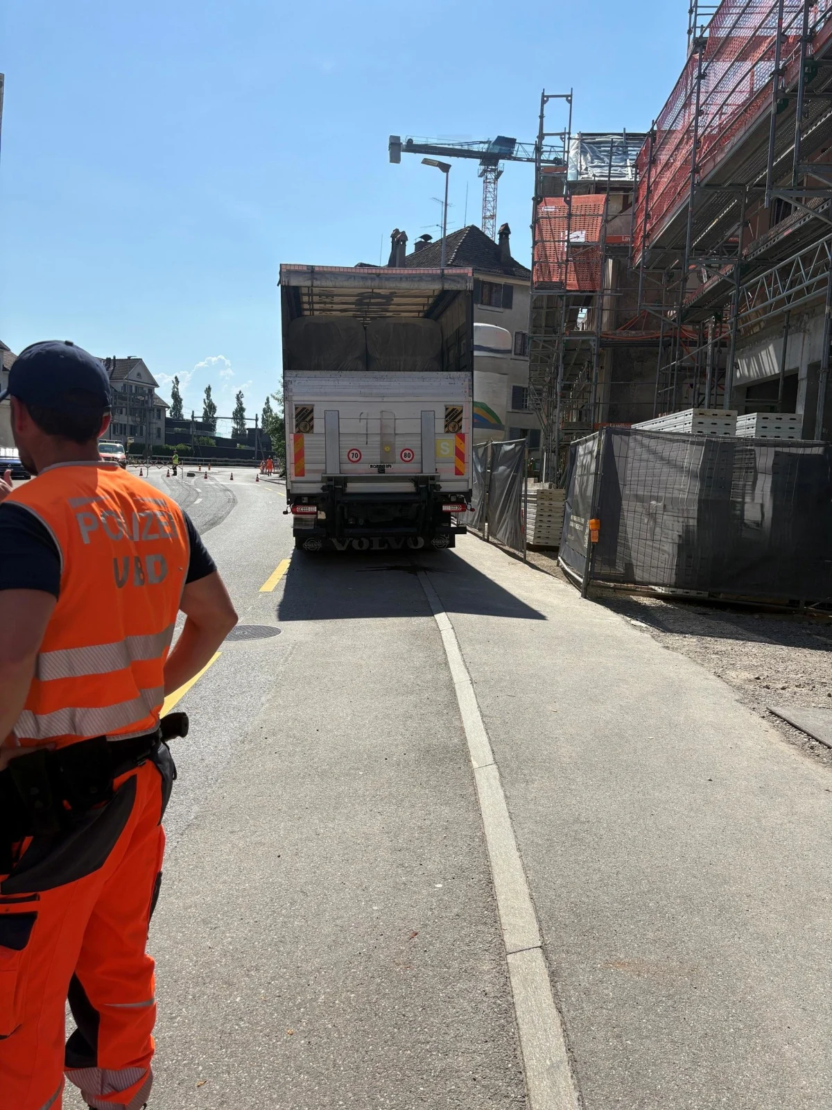 Ein Polizist in Warnweste steht neben einem Lastwagen auf einer Straße mit Baustelle, es ist sonnig und klar.