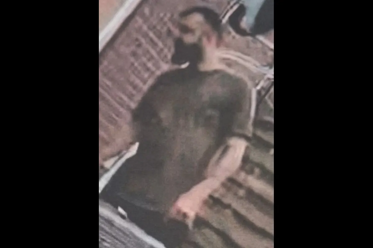 Ein unscharfes Bild zeigt eine Person, die vor einer Treppe und einer Ziegelmauer steht. Die Person ist nicht erkennbar.