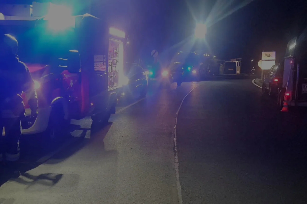 Mehrere Einsatzfahrzeuge stehen mit eingeschaltetem Blaulicht auf einer Landstraße bei Nacht. Im Vordergrund ist ein Feuerwehrfahrzeug sichtbar.