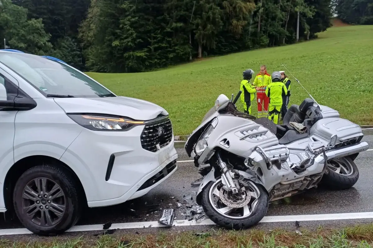 Ein silbernes Motorrad liegt beschädigt auf einer Landstraße, nachdem es mit einem weißen Lieferwagen kollidiert ist. Im Hintergrund stehen mehrere Personen in Sicherheitskleidung auf dem Rasen.
