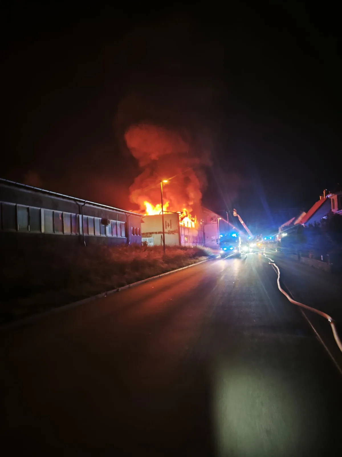 Ein Gebäudekomplex steht in hellen Flammen, während Feuerwehrfahrzeuge mit eingeschaltetem Blaulicht vor Ort sind.