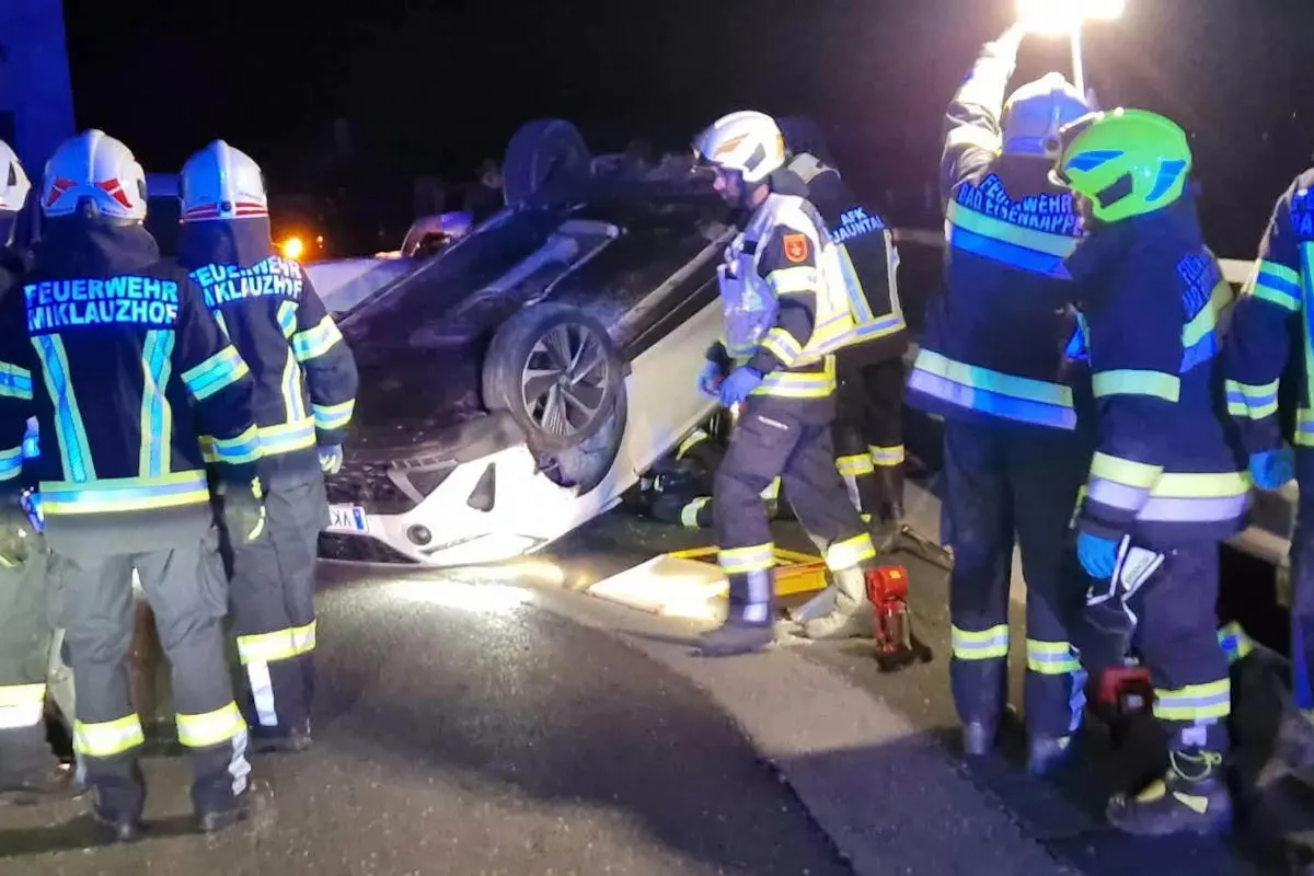 Mehrere Feuerwehrleute sind bei der Bergung eines auf dem Dach liegenden Fahrzeugs auf einer Straße im Einsatz.
