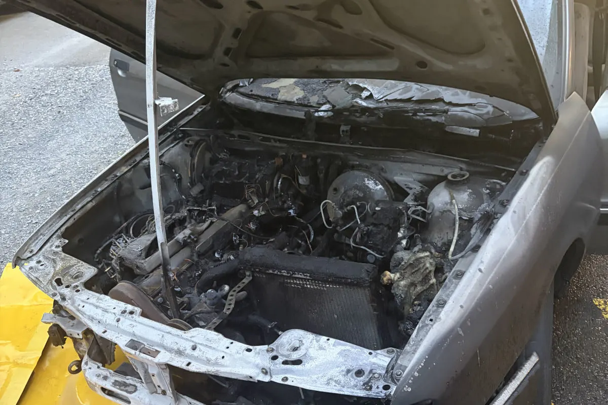 Ein Auto mit geöffneter Motorhaube zeigt einen stark beschädigten Motorraum. Sichtbar sind Verbrennungen und Verkohlungen.