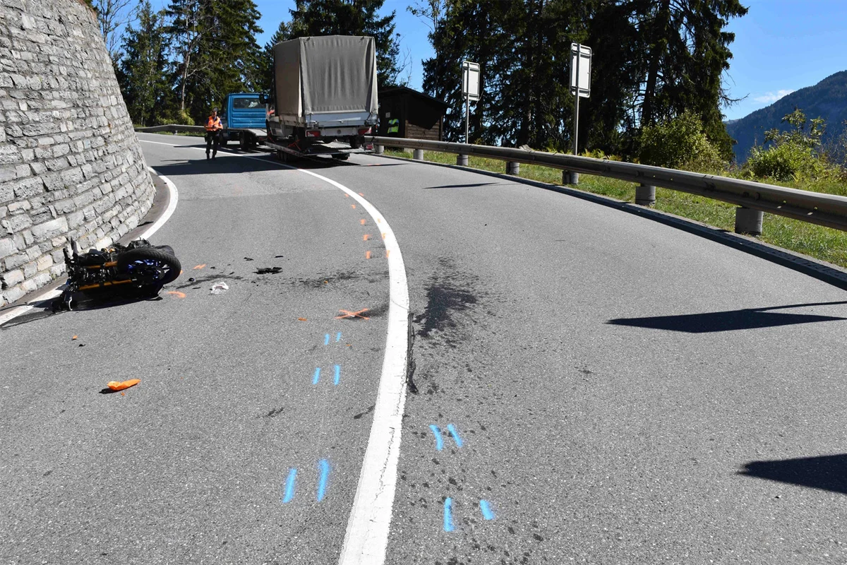 Ein beschädigtes Motorrad liegt auf einer Bergstraße in einer Kurve. Ein Lastwagen steht weiter hinten, während ein Polizeibeamter Aufzeichnungen macht.