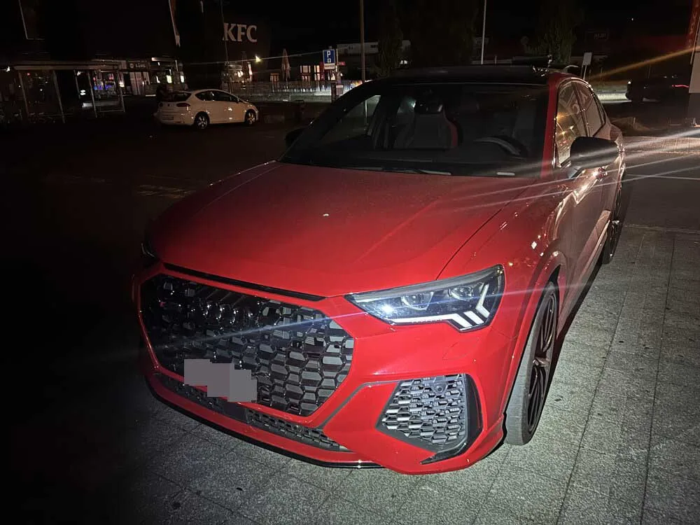 Ein rotes Audi-SUV ist bei Nacht auf einem Parkplatz abgestellt. Im Hintergrund sind ein KFC-Gebäude und weitere Fahrzeuge sichtbar.