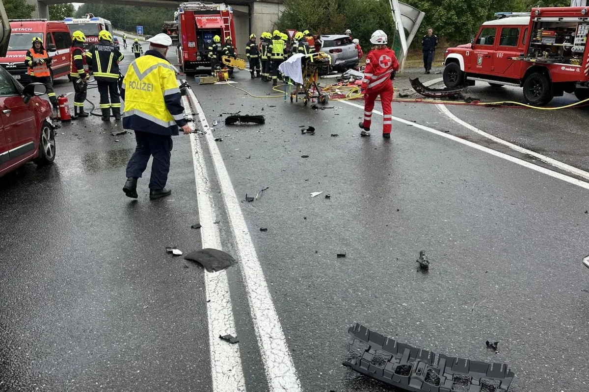 Einsatzkräfte arbeiten an der Unfallstelle auf einer nassen Straße. Wrackteile liegen verstreut; mehrere Einsatzfahrzeuge sind vor Ort.
