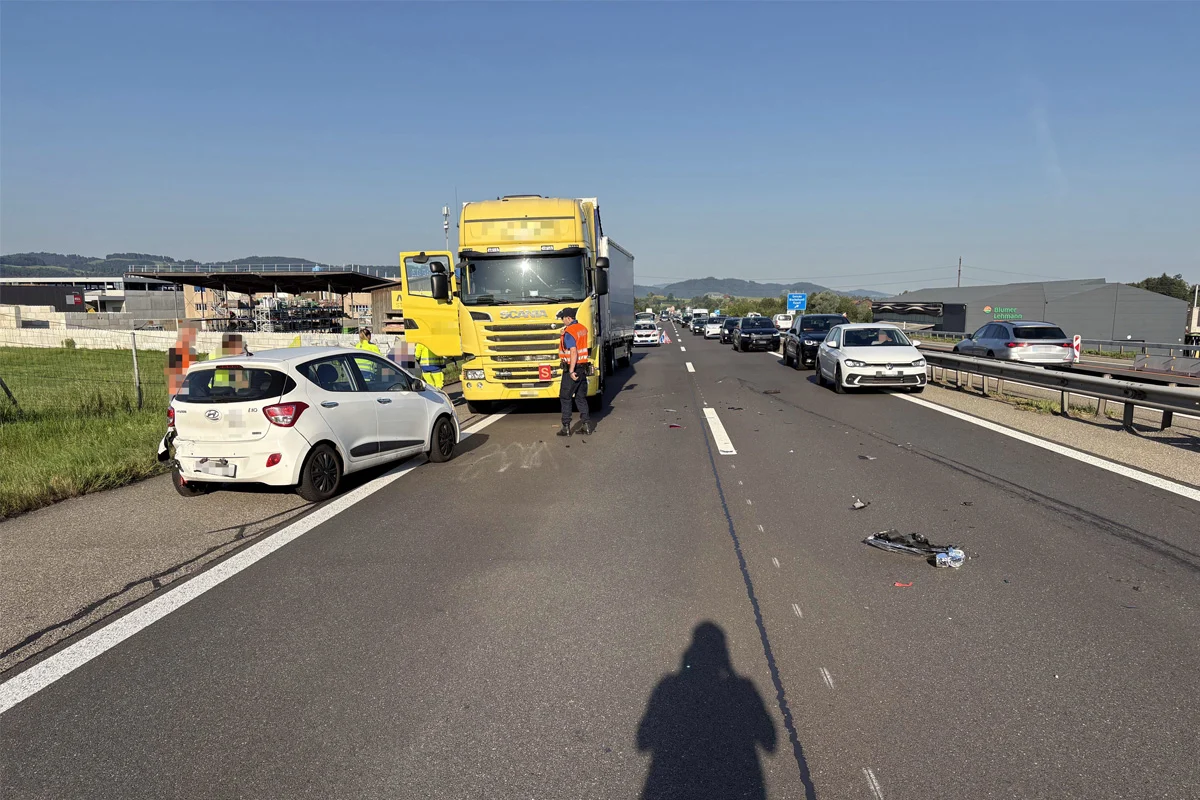 Ein weißer Hyundai mit Heckschaden steht auf der Autobahn neben einem gelben Lastwagen. Im Hintergrund staut sich der Verkehr.