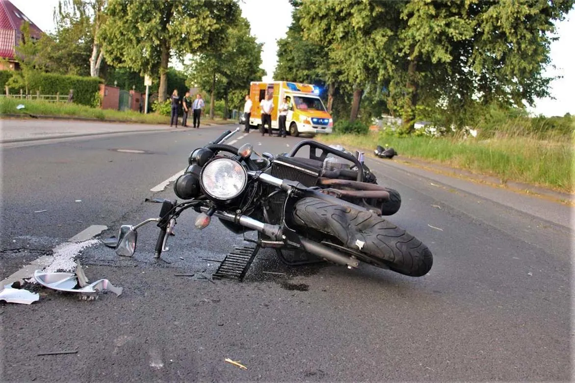 Ein Motorrad liegt nach einem Unfall auf der Straße, im Hintergrund ein Krankenwagen mit eingeschaltetem Blaulicht und mehrere Personen.