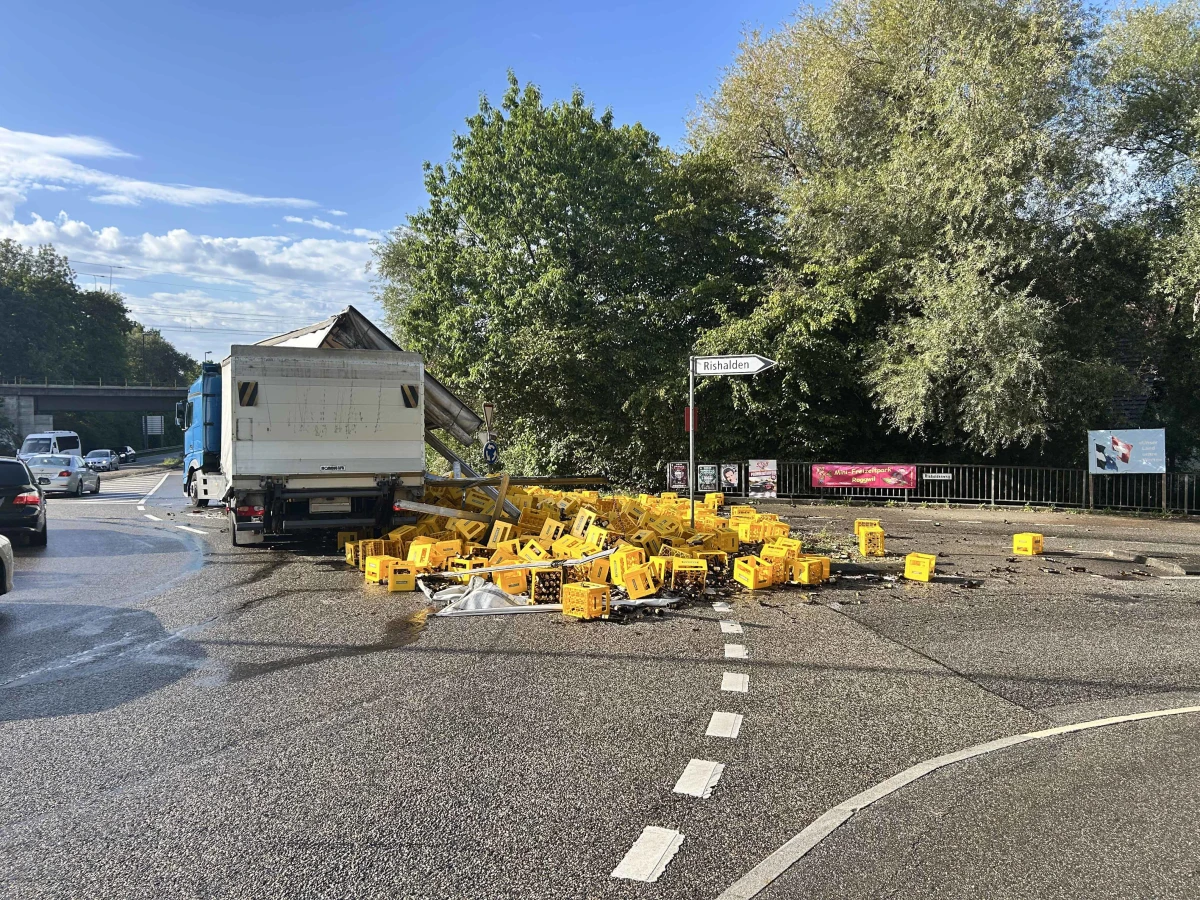 Ein umgekippter Lkw hat zahlreiche gelbe Getränkekisten auf die Straße gestreut, die unter einem klaren Himmel liegt.