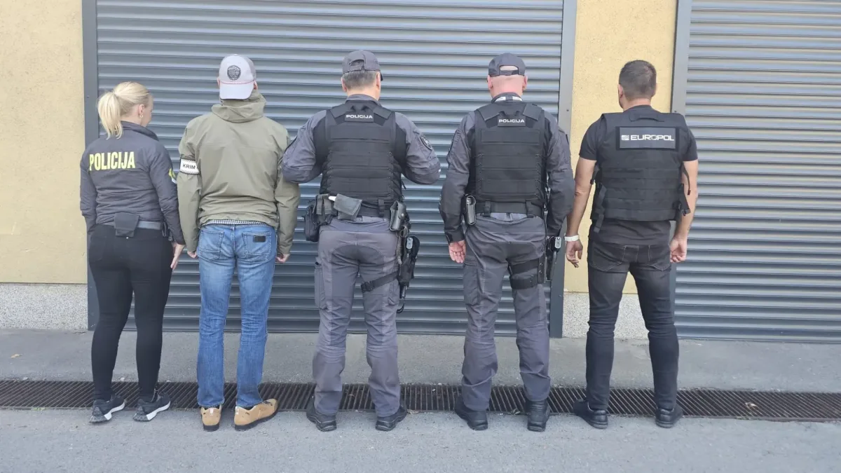 Fünf Personen, zwei in Polizeiausrüstung und drei zivil gekleidete, stehen mit dem Rücken zu einem geschlossenen Rolltor.