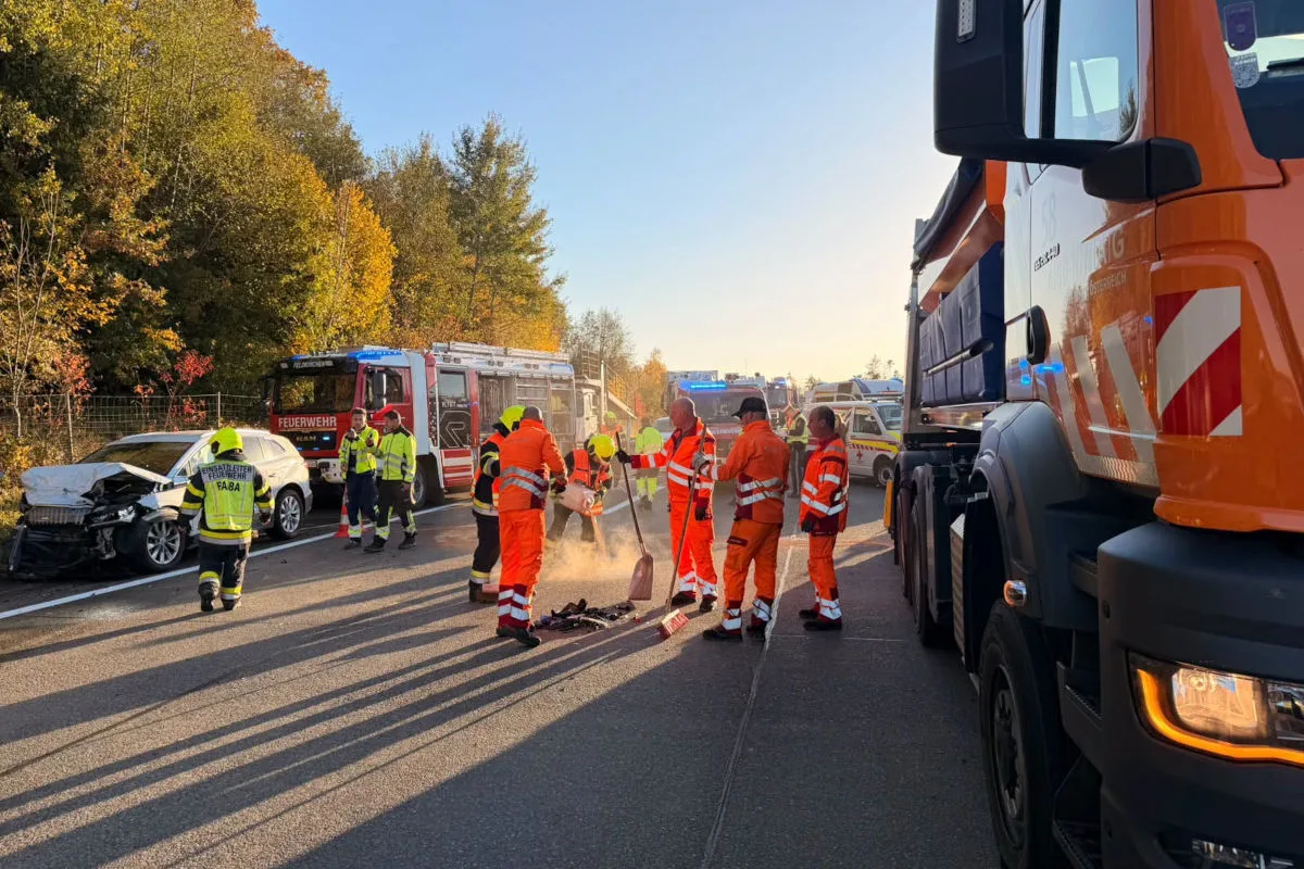 Mehrere Feuerwehrleute stehen an einer Unfallstelle neben einem weißen, beschädigten Auto. Im Hintergrund sind Einsatzfahrzeuge sichtbar.