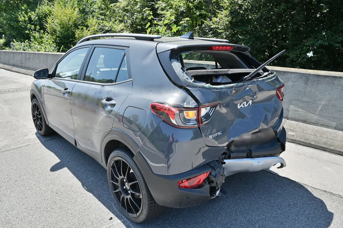Ein grauer SUV mit einem stark beschädigten hinteren Teil und zerbrochener Heckscheibe steht am Straßenrand. Die Karosserie ist eingedrückt.