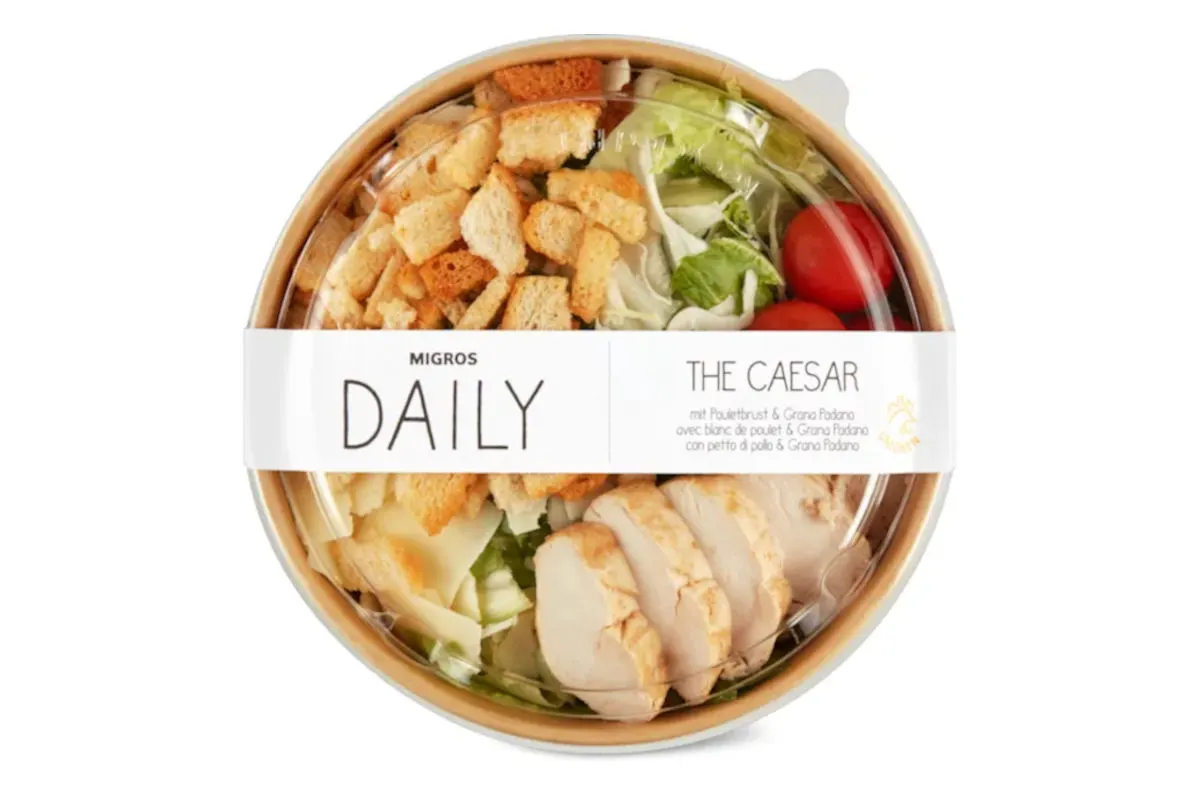 Ein verpackter Caesar-Salat in einer Plastikschale mit Croutons, Hühnchenstreifen und Kirschtomaten ist zu sehen.