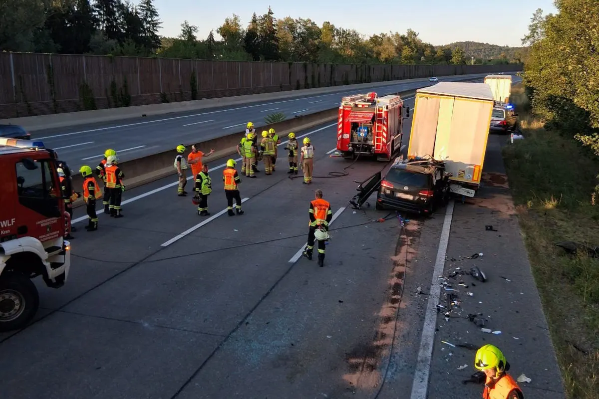 Auf der Autobahn sind Feuerwehrleute und Rettungskräfte bei einem Unfall im Einsatz, bei dem ein Pkw auf einen Lkw geprallt ist. Trümmer liegen auf der Fahrbahn, umgeben von Einsatzfahrzeugen und Personal.