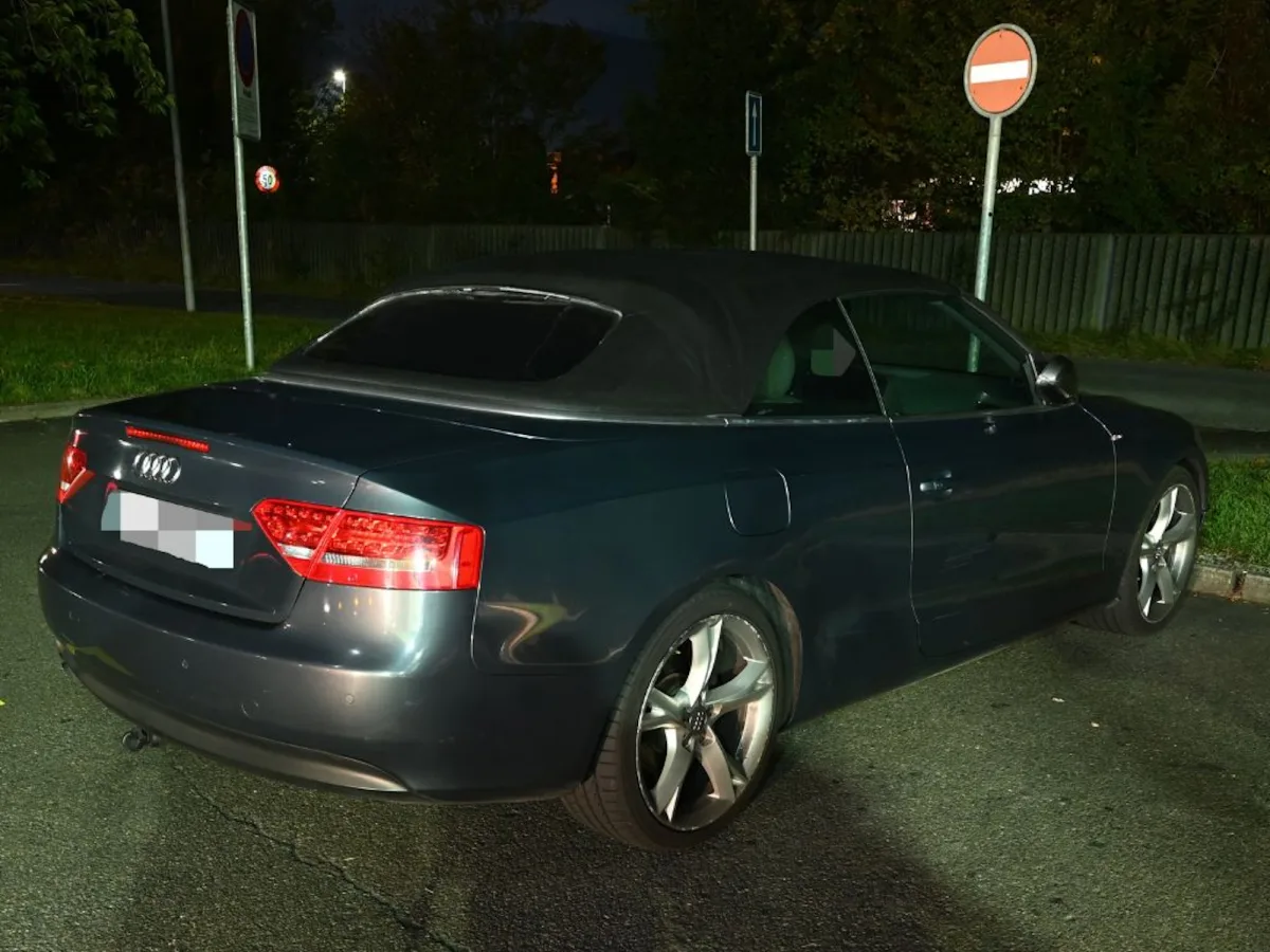 Ein schwarzes Audi-Cabriolet steht bei Nacht auf einem Parkstreifen. Im Hintergrund sind Verkehrsschilder erkennbar.