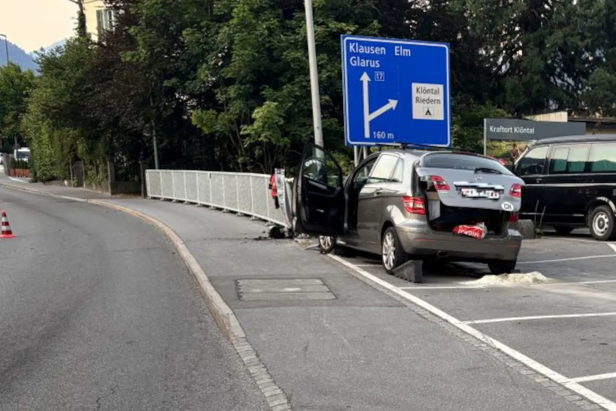 Ein graues Auto mit offenen Türen steht nah an der Straße. Ein blaues Wegweiser-Schild zeigt die Richtung nach Klausen und Elm.