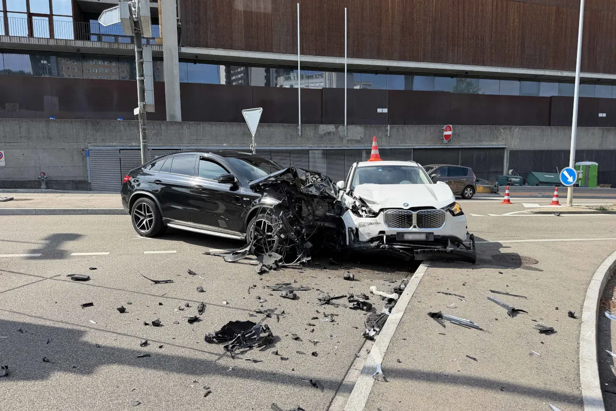 Ein schwarzes und ein weißes Auto sind frontal an einer Kreuzung kollidiert. Um sie herum liegen zahlreiche Trümmerteile auf der Fahrbahn.